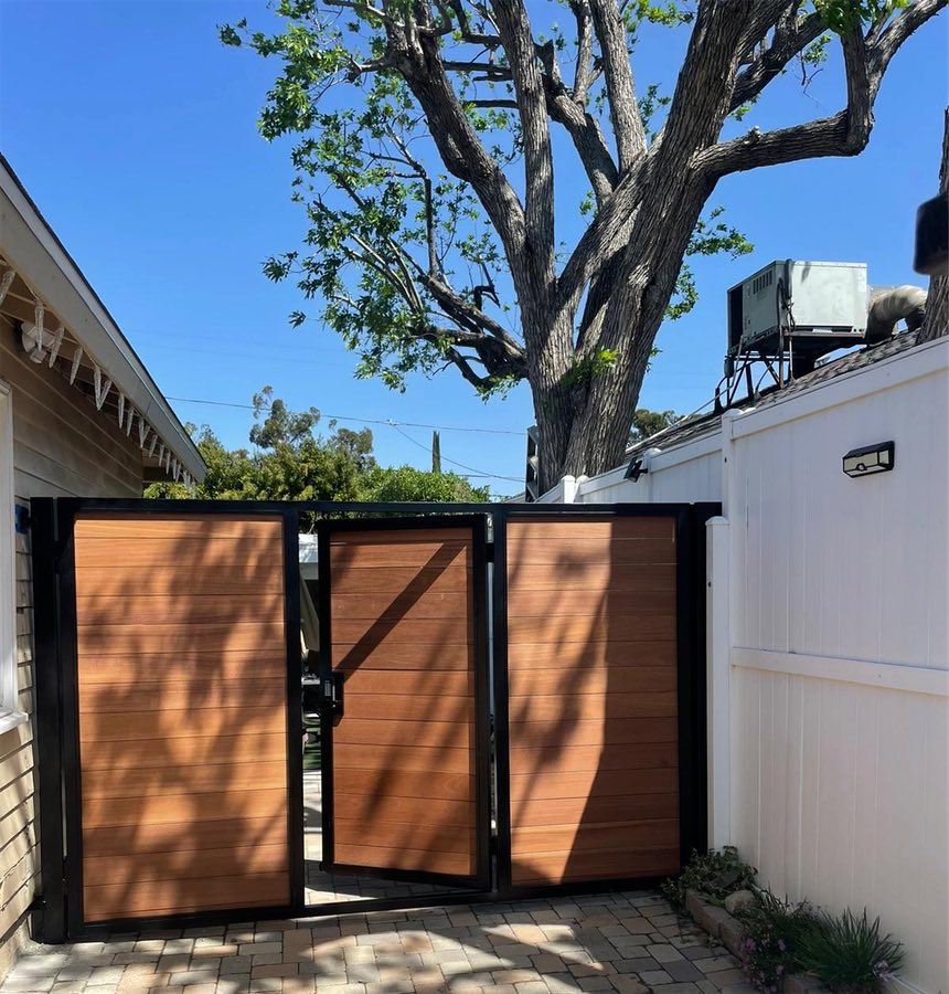 A horizontal slat gate in a black frame between a house and a white fence