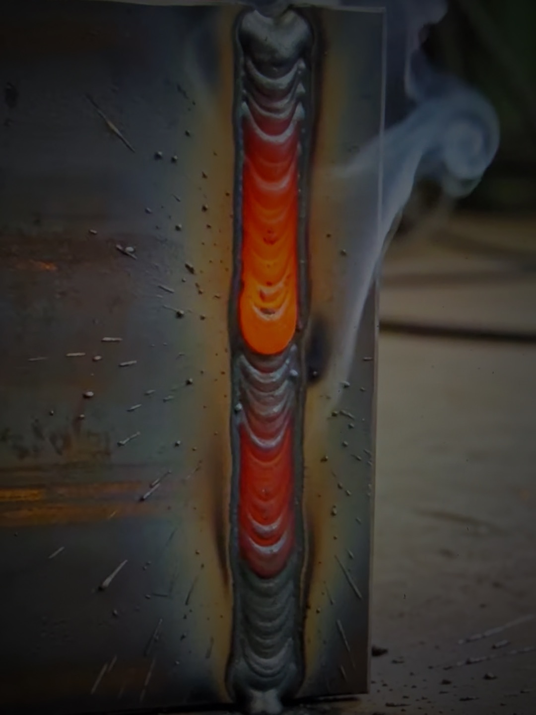 A freshly welded seam on a steel plate, still glowing red, with smoke curling off it