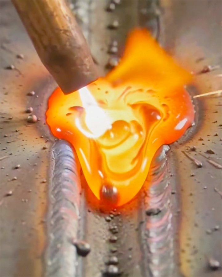 A weld pool glowing orange under the welding torch, between two finished beads