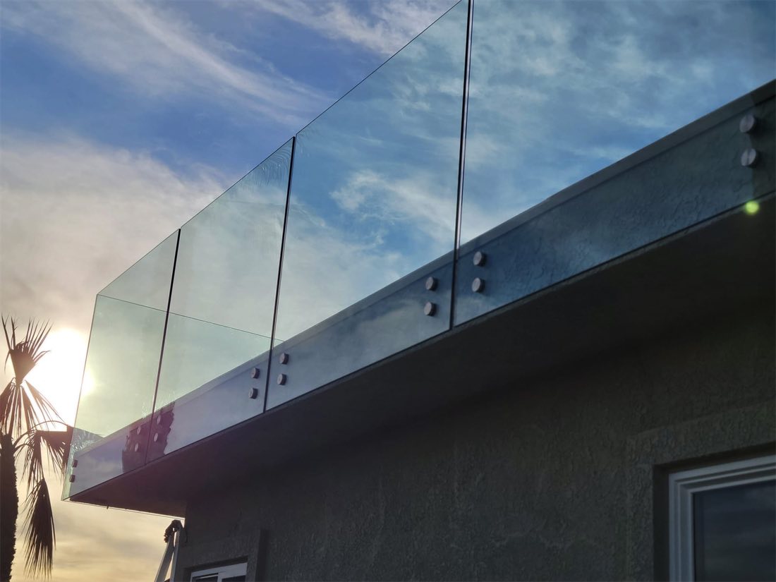 Glass railing panels fixed to the face of a roof edge, seen from below against the sky