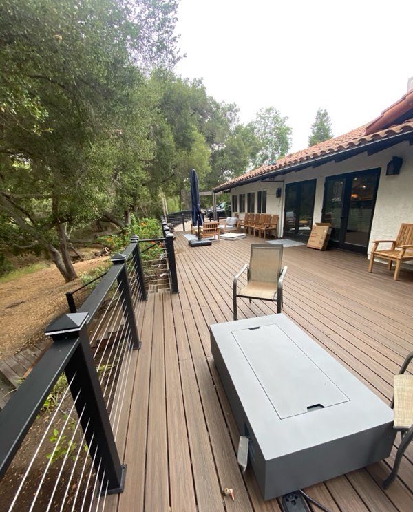 A cable railing with black posts along a wooden deck beside a house