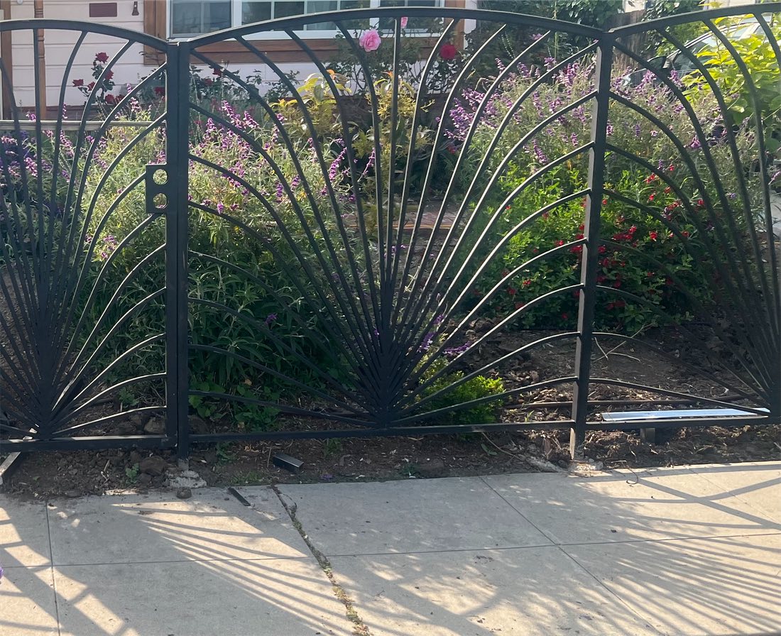 An ornamental fence with fan-shaped bars in front of a flower garden