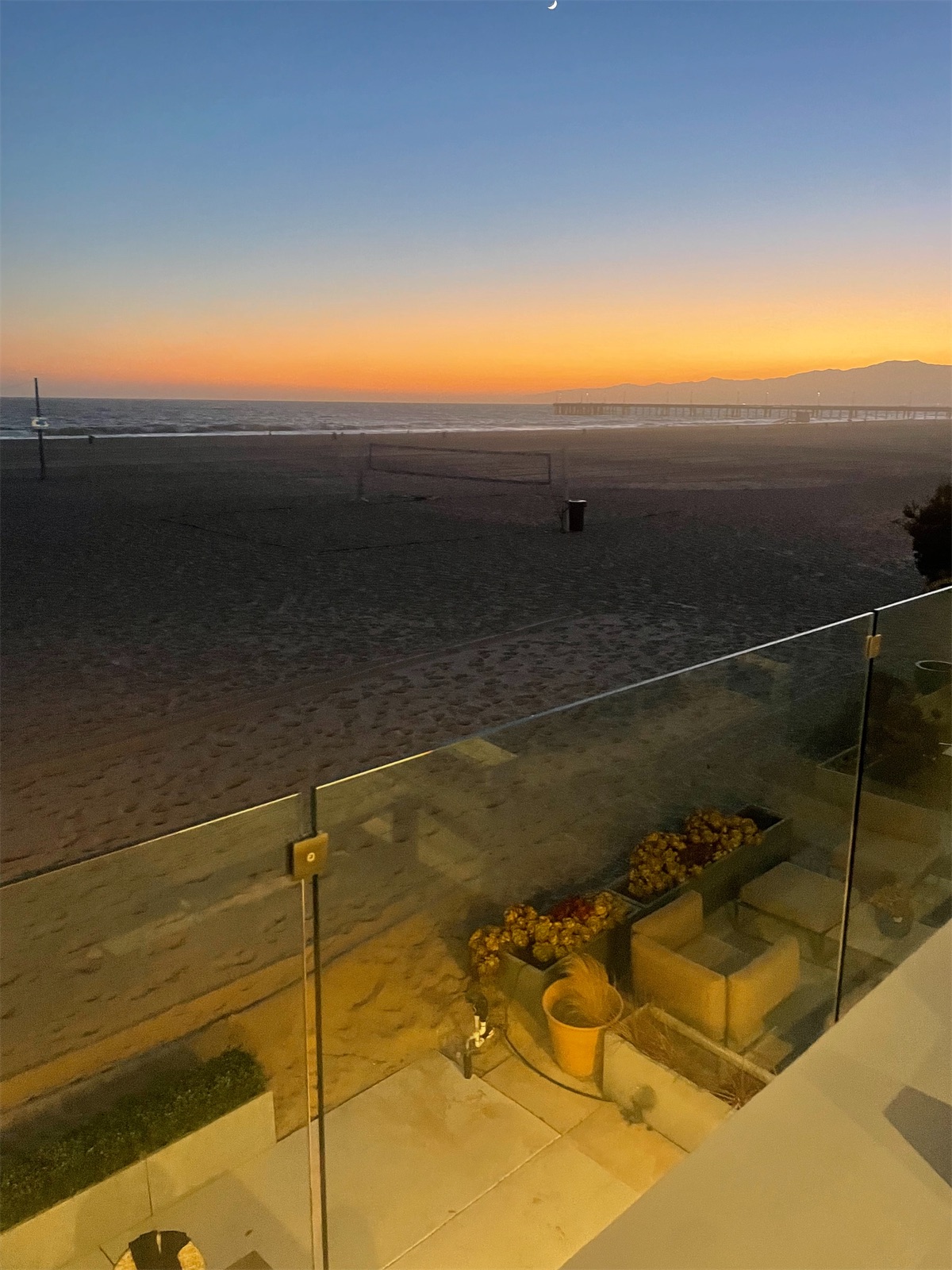 The sun going down over the beach, seen across a glass terrace railing