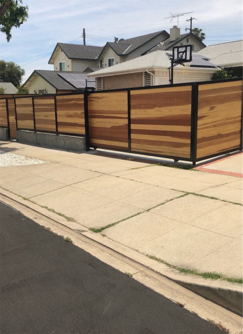 A horizontal slat fence with black posts along a residential sidewalk