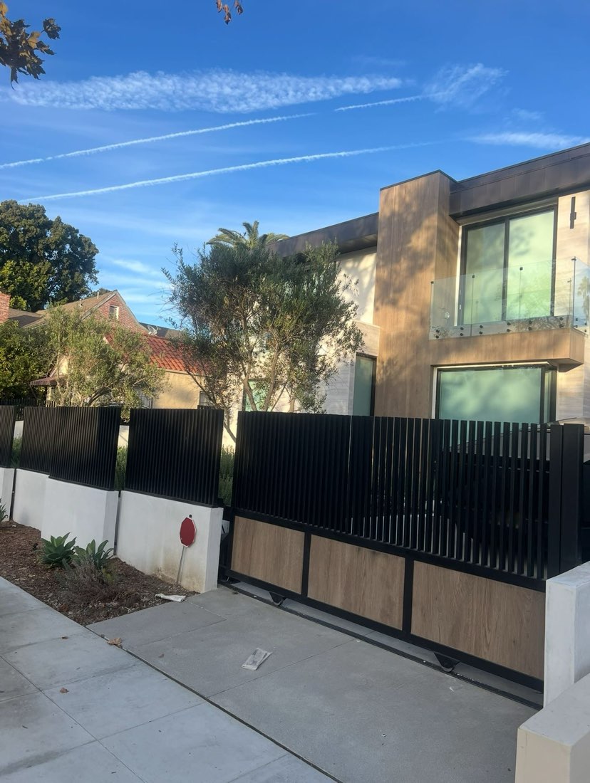 A driveway gate and vertical bar fence set on white walls in front of a modern home